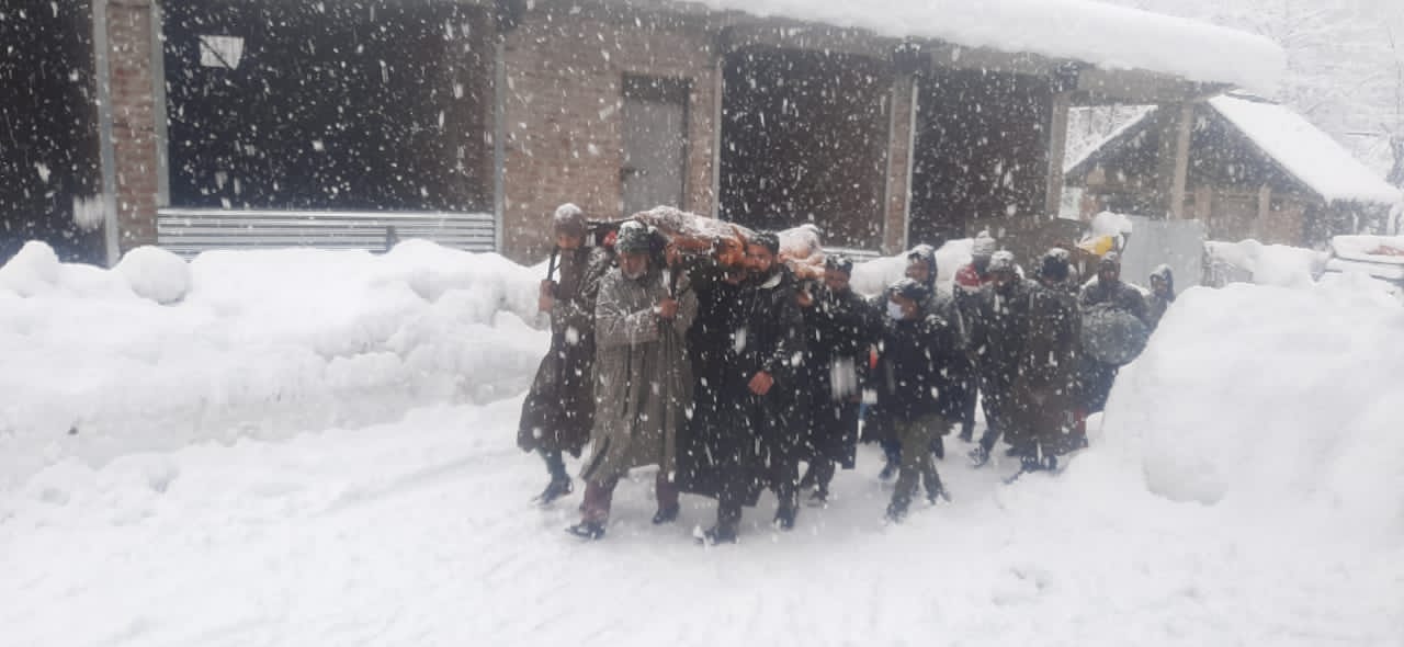 Amid snowfall, local Muslims walk on foot to shoulder the dead body of a Pandit stuck in an ambulance in South Kashmir